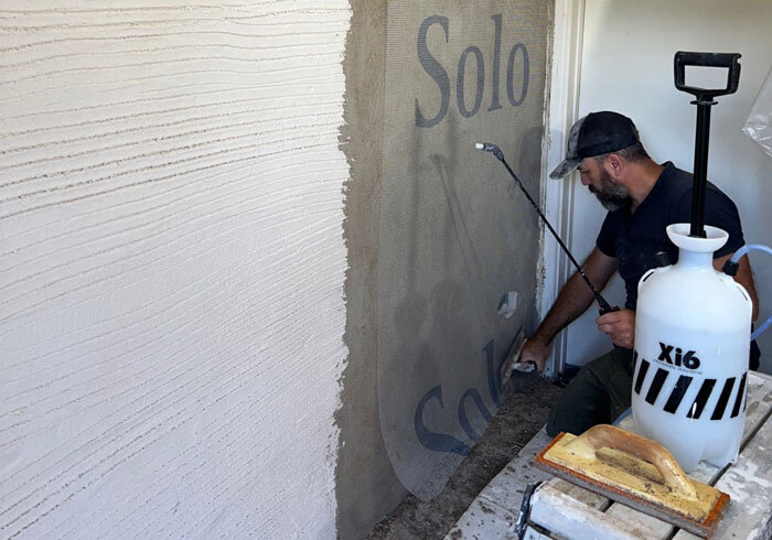 Adding the mesh layer shows the plasterer pressing the render mesh into the first layer of Supertherm Topcoat
